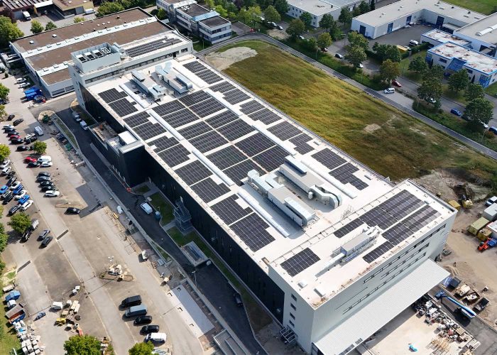 Solaranlage-auf-Industriehalle-flachdach-nachhaltige-Stromversorgung-im-GewerbeMySolarMontage Luftaufnahme einer Industriehalle mit großflächiger Photovoltaikanlage auf dem Flachdach zur nachhaltigen Stromversorgung im Gewerbegebiet.